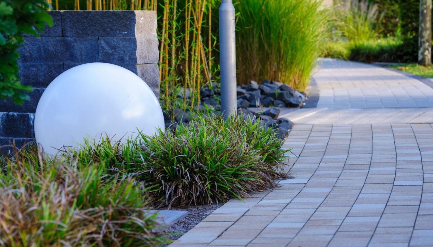 Gepflasterter Gartenweg mit Kugelleuchte und Ziergräsern