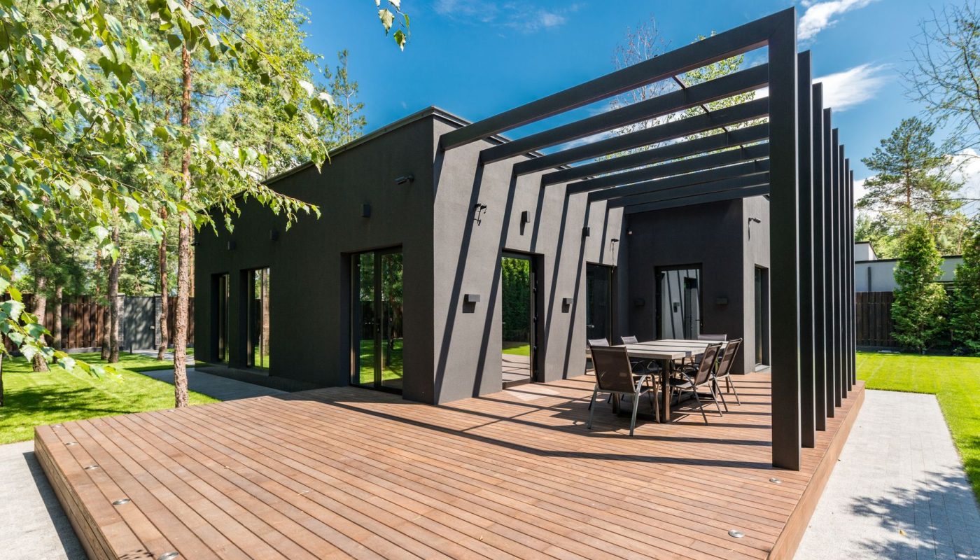 Große Holzterrasse mit dunkler Pergola vor einem modernen Haus im gepflegten Garten
