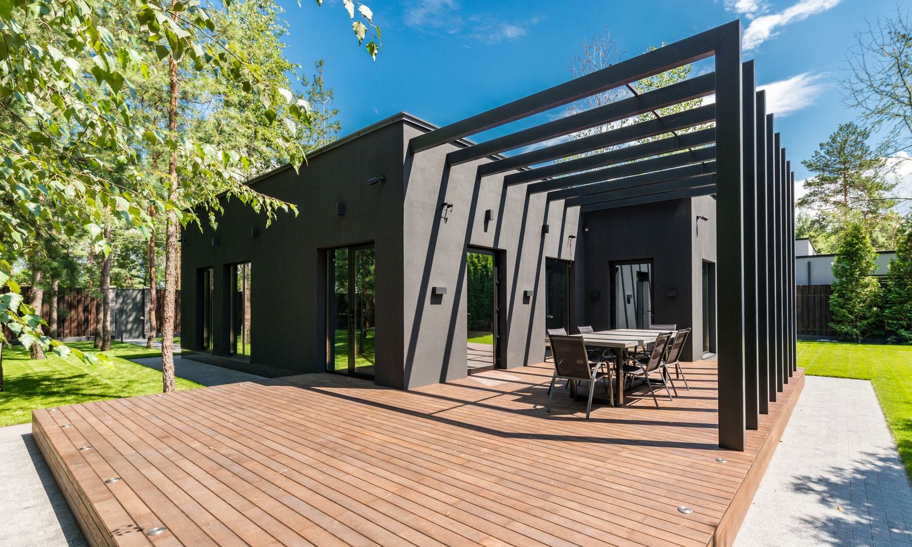 Große Holzterrasse mit dunkler Pergola vor einem modernen Haus im gepflegten Garten
